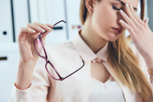 Tired businesswoman holding eyeglasses and massaging nose bridge. Girl feeling discomfort from long wearing glasses at workplace. Exhausted female office worker gather herself for completing work